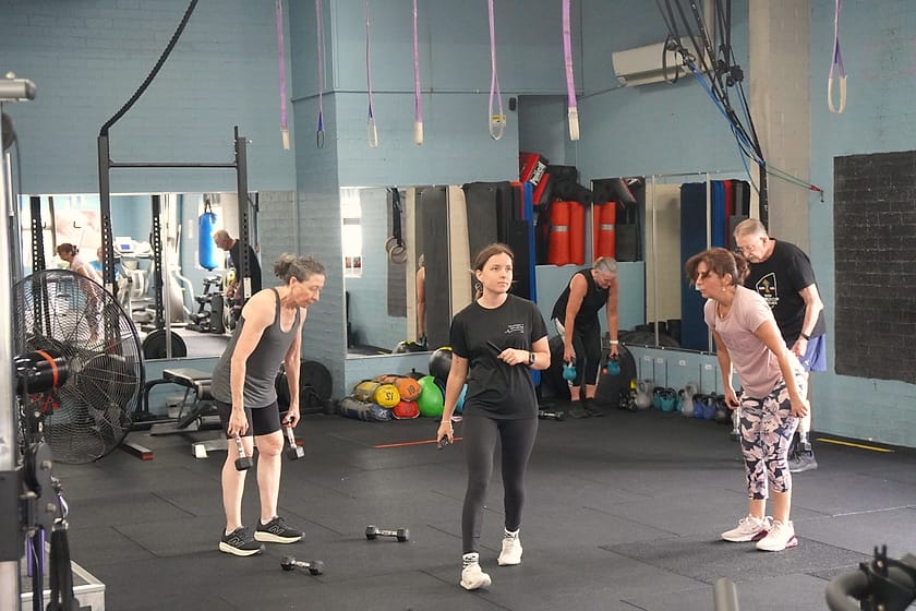 A coach taking two members through a strength set in the Solutions4Wellbeing gym